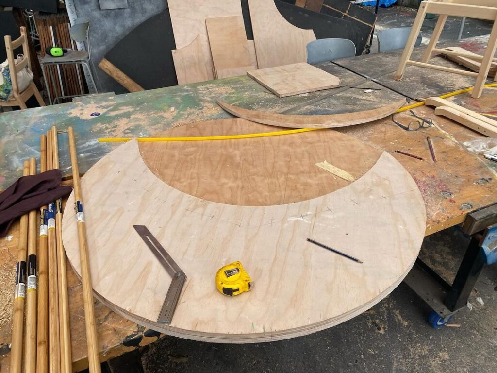 A woodworking shop with various tools and a large, circular wooden panel marked for cutting on a workbench. A woodworking shop with various tools and a large, circular wooden panel marked for cutting on a workbench.