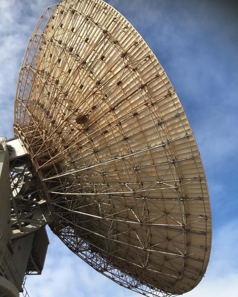 Large satellite dish with a lattice structure, viewed from below against a partly cloudy sky. Large satellite dish with a lattice structure, viewed from below against a partly cloudy sky.