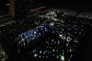 Two people lie on black mats in a dark room, illuminated by scattered light spots resembling stars or a digital projection.