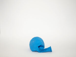 A deflated blue balloon lies on a plain white background.