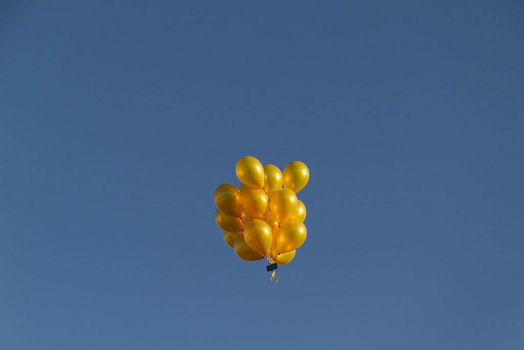 A cluster of yellow balloons floats high in a clear blue sky.