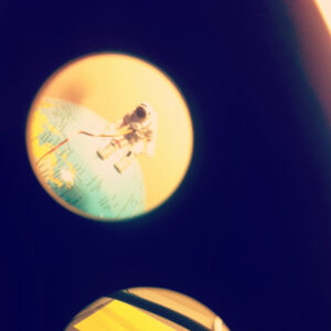 A small astronaut figurine stands on a globe, viewed through a circular frame with another out-of-focus circle below.